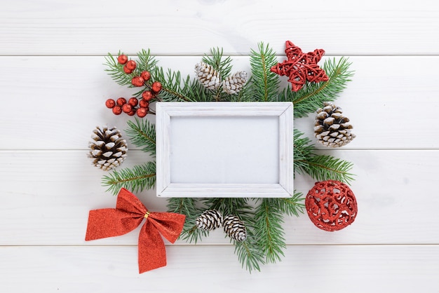 Marco de fotos con decoración de Navidad, con lazo de cinta roja y piñas en una mesa de madera blanca. Vista superior, marco para copiar espacio