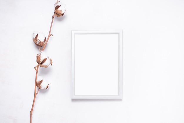 Marco de fotos decorado con rama de flor de algodón sobre fondo blanco de madera