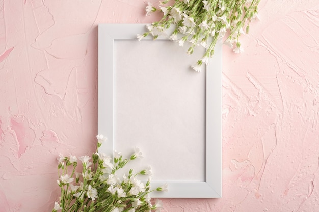 Marco de fotos vacío blanco con flores de pamplina oreja de ratón sobre fondo rosa, espacio de copia de vista superior