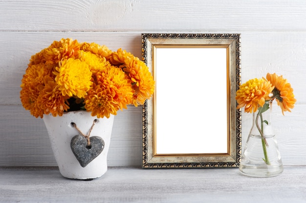 Marco de fotos vacío y flores de crisantemo naranja sobre mesa rústica blanca