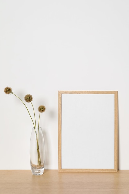 Marco de fotos vacío y jarrón con flores decorativas secas sobre mesa de madera Mockup para diseño