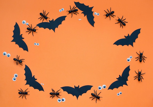 Marco de Halloween con decoraciones negras sobre un fondo naranja Hormigas y ojos de murciélago de papel negro