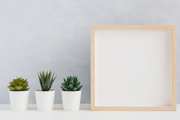 Foto marco de madera en blanco con tres tipos de planta de cactus en maceta en el escritorio