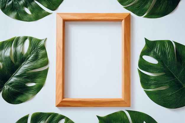 Marco de madera decorado con hojas tropicales Monstera sobre fondo blanco.