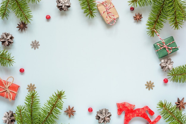 Marco de Navidad hecho de ramas de abeto, frutos rojos, cajas de regalo, juguete retro y conos de pino sobre fondo azul. Fondo de Navidad. Endecha plana. vista superior con espacio de copia