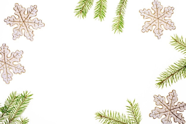 Marco navideño hecho de copos de nieve decorativos y ramitas de abeto verde sobre fondo blanco Copiar espacio
