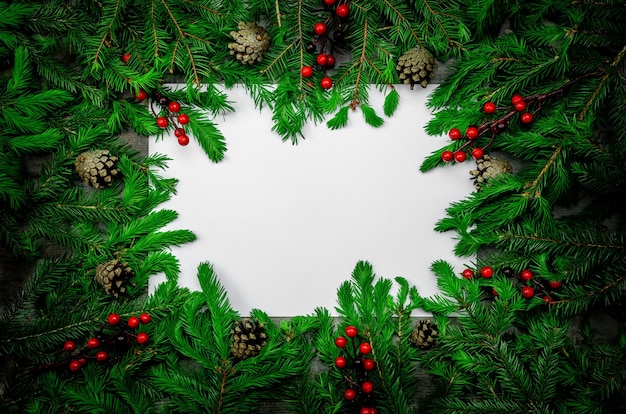 Marco navideño hecho de ramas de abeto oscuro conos bayas rojas y decoraciones fondo blanco para texto Feliz Navidad y feliz año nuevo