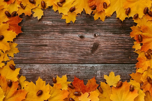 Marco de otoño de hojas de arce y bellotas en el fondo de tablas de madera