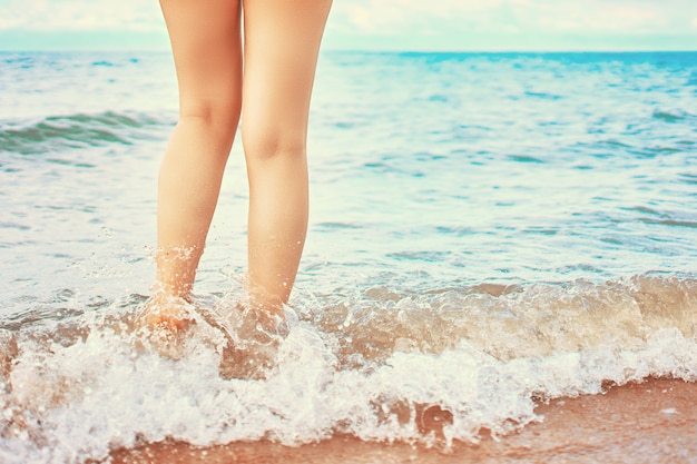 En el marco de los pies de una mujer caminando en la playa junto al mar en un día soleado