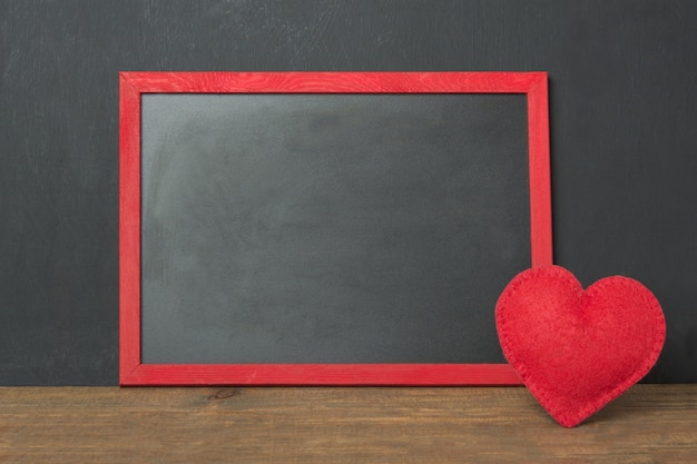 Marco de pizarra con lugar para el texto y corazón de fieltro rojo como decoración en la mesa de madera. Tarjeta de San Valentín .