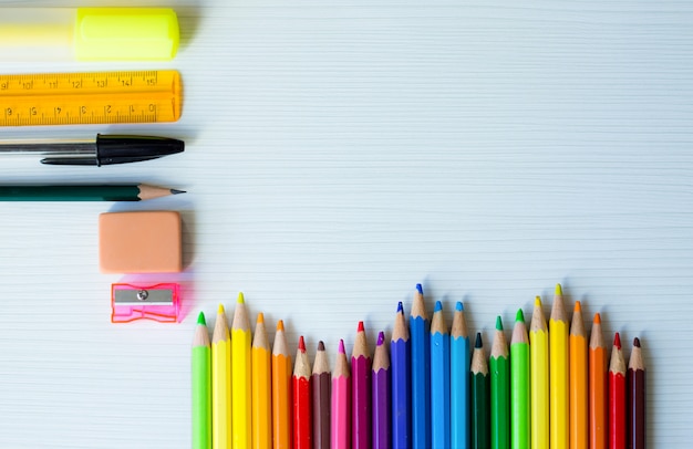 Marco de regreso a la escuela con arcoiris de bolígrafos de colores y otros útiles escolares y fondo de madera blanca