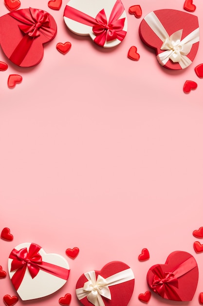 Marco romántico de San Valentín de regalos con corazones rojos sobre fondo rosa. Endecha plana. Tarjeta de felicitación vertical con espacio de copia.