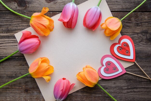 Marco de tulipán con dos corazones y papel sobre fondo de madera