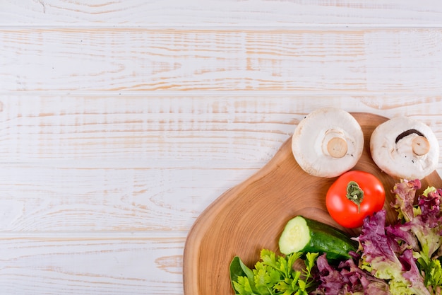 Foto marco de verduras frescas, lechuga, tomate, pepino, champiñones, perejil, espinacas en madera