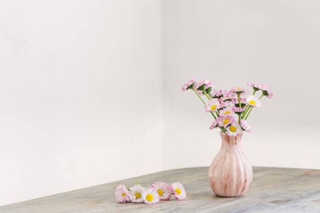 Margarida com flores em um vaso rosa na mesa de madeira