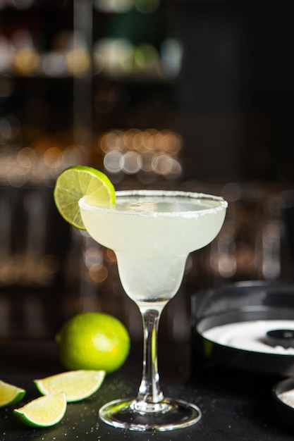 Margarita en un vaso con limón en un vidrio con nueces y verduras de fondo oscuro
