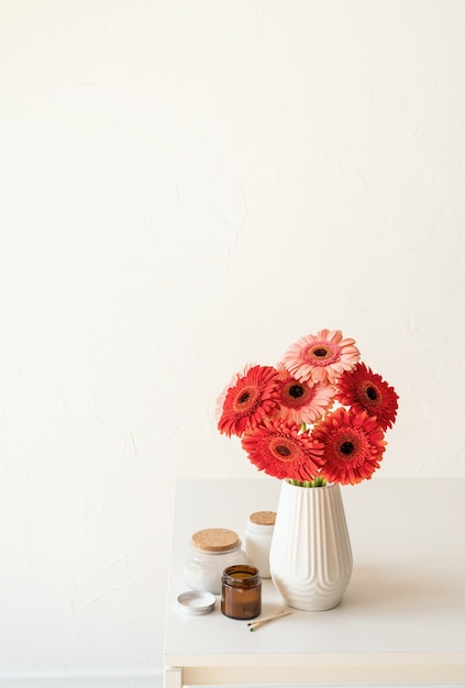 Margaritas gerberas rojas y rosadas en jarrón blanco sobre la mesa de la cocina y el fondo de la pared blanca