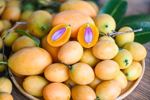 Marianische Pflaumenfrucht und -blätter in der Platte auf hölzernem Hintergrund tropische Frucht Name in Thailand Sweet Yellow Marian Plum Maprang Plango oder Mayong chid