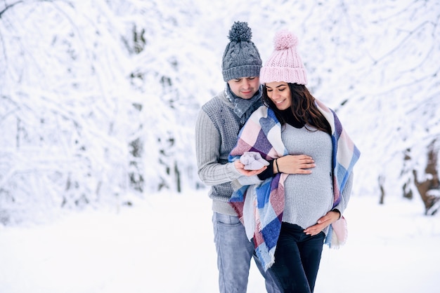 Marido abraçando ternamente sua linda esposa grávida em um parque de inverno nevado
