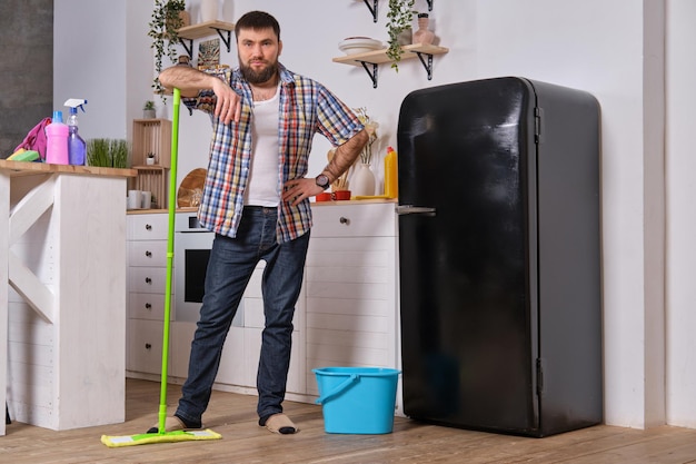 Marido ama de llaves limpia la cocina joven feliz con trapeador verde lava el piso