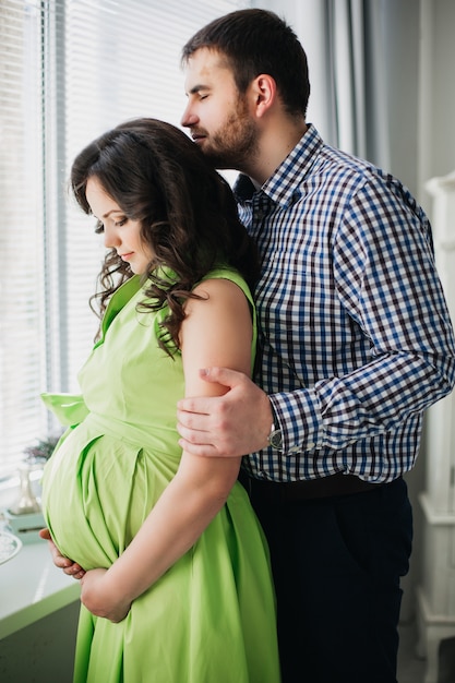 Foto marido amoroso abrazando a su esposa embarazada en vestido verde