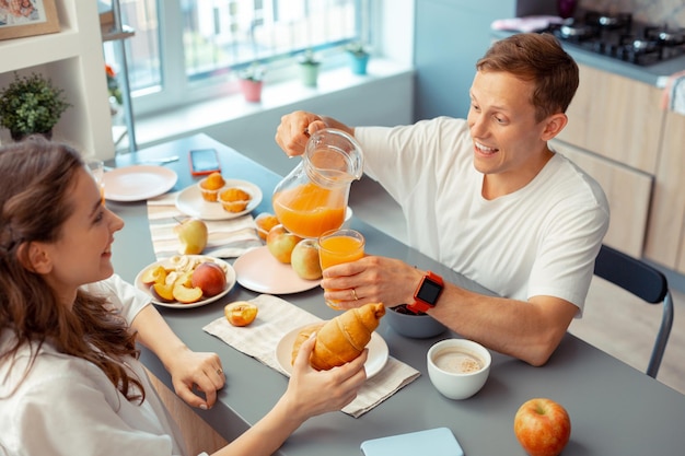 Marido cariñoso sirviendo un poco de jugo para su esposa comiendo croissant