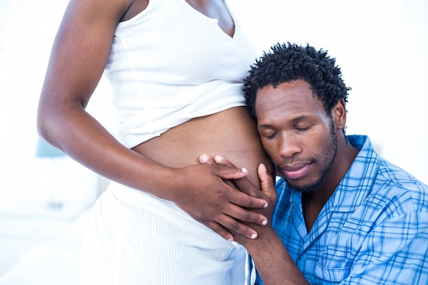 Marido com olhos fechados ouvindo sua esposa grávida