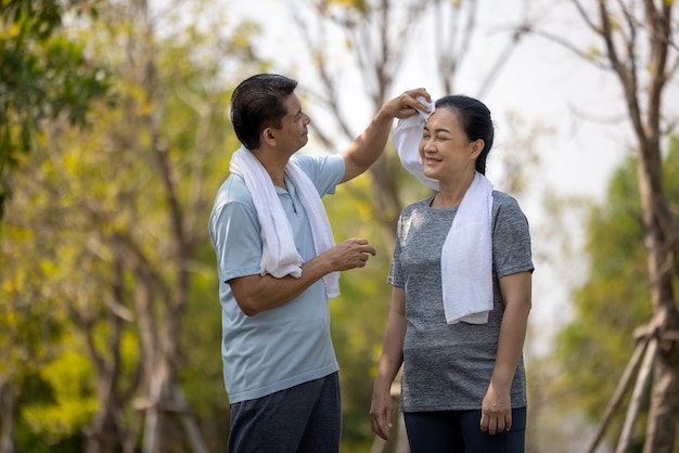 Marido de casal sênior feliz asiático enxugando o suor do rosto da esposa depois de correr no parque ao ar livre.