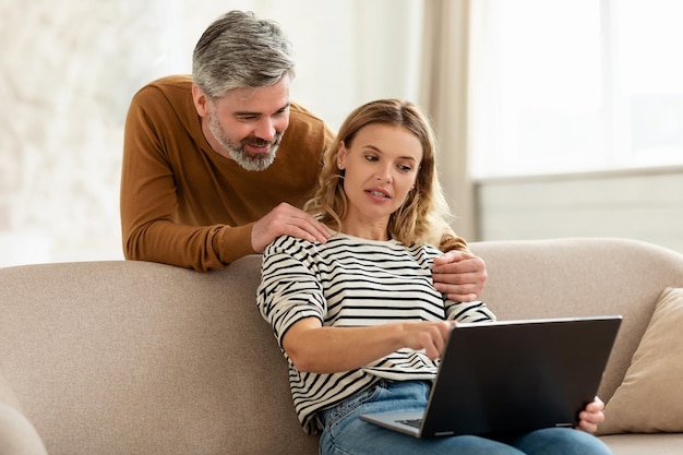 Marido e esposa de meia-idade usando laptop navegando na internet interna