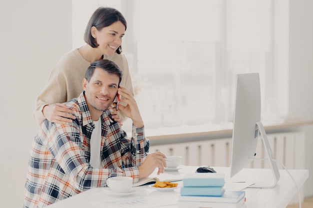 Marido e esposa felizes fazem a papelada juntos pagam impostos on-line olham para a tela do computador posam na área de trabalho com livros e papéis bebem café e almoçam fazer chamadas telefônicas via smartphone