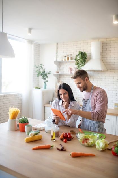 Marido e mulher assistindo a um vídeo de culinária e cozinhando antes do almoço