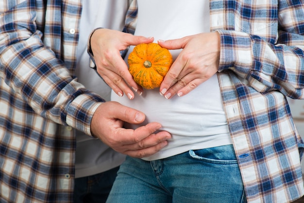 Marido e mulher de jeans e camisa xadrez segurando uma pequena abóbora nas mãos