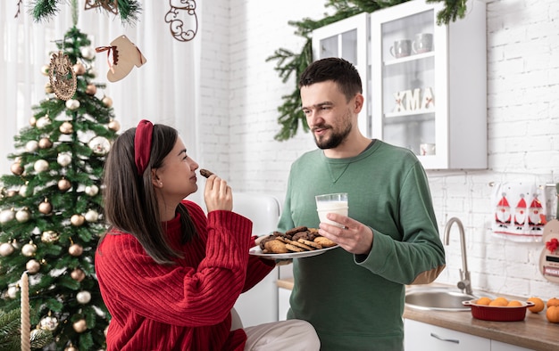 Marido e mulher felizes com biscoitos de natal e leite na cozinha