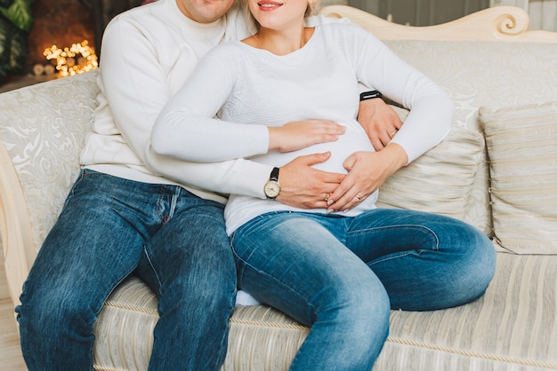 Marido e mulher grávida, sentado com as mãos na barriga.