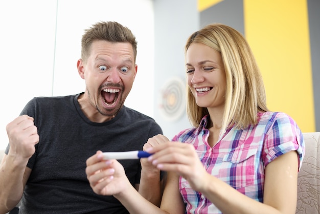 Marido e mulher sorrindo estão olhando para o teste de gravidez