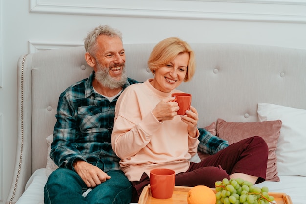 Marido e mulher tomam café da manhã na cama com café e frutas