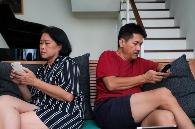 Marido y esposa sentados espaldas en el sofá ignorándose el uno al otro y ocupados con sus propios teléfonos celulares
