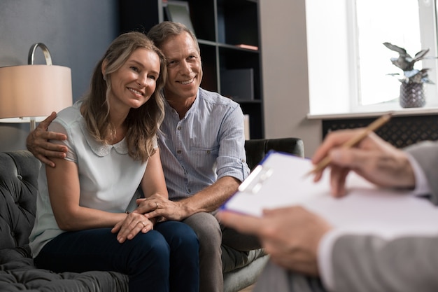 Marido feliz abraçando sua esposa sorridente enquanto está sentado no sofá na frente de um psicanalista