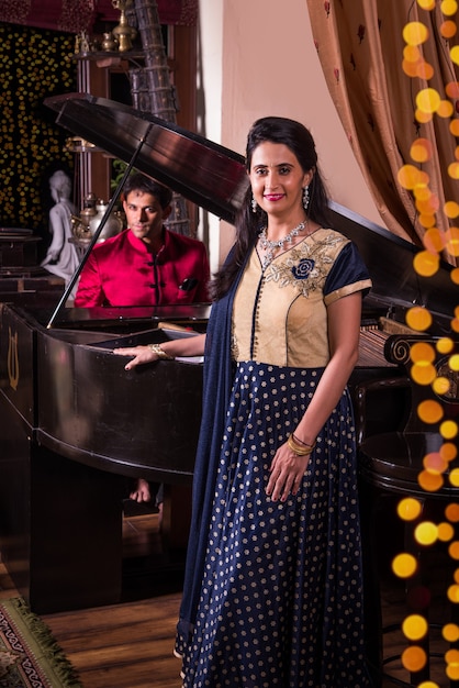 Marido indio tocando el piano para esposa. Mujeres felices disfrutando de la música interpretada por el marido sobre el piano de cola