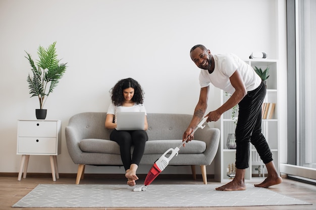 Marido limpando com aspirador enquanto esposa trabalhando no laptop