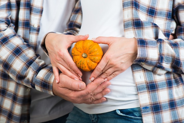 Foto marido y mujer en jeans y una camisa a cuadros tiene una pequeña calabaza en sus manos