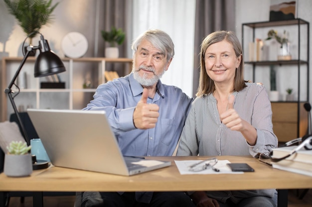 Marido y mujer mayores que muestran los pulgares para arriba gesto en el trabajo