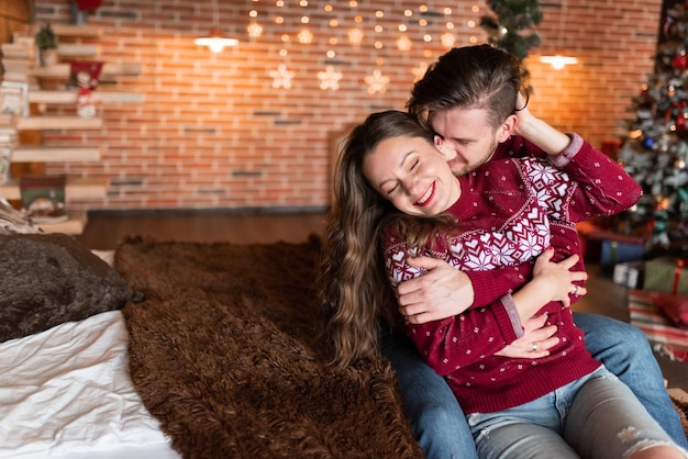 Marido y mujer con suéteres de punto idénticos se divierten juntos celebrando la Navidad Pareja juntos en la cama Los amantes están en una habitación estilo loft bellamente decorada