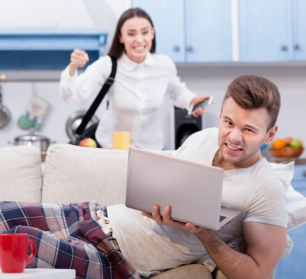 Marido preguiçoso no sofá e sua esposa furiosa, que vai trabalhar.