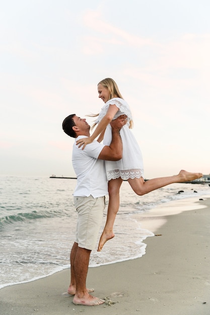 Marido segurando a esposa na praia perto do oceano ao pôr do sol. casal romantico