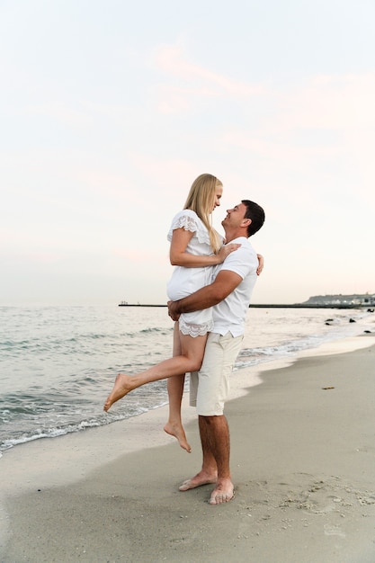 Marido segurando a esposa na praia perto do oceano ao pôr do sol. casal romantico