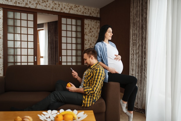 Marido y su esposa embarazada con el vientre relajándose en casa. Embarazo, período prenatal. La futura mamá y el papá están descansando, atención médica