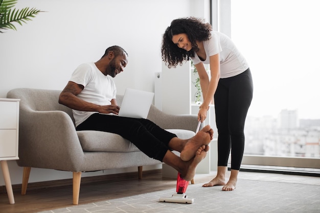 Marido trabalhando no laptop enquanto a esposa aspira o chão