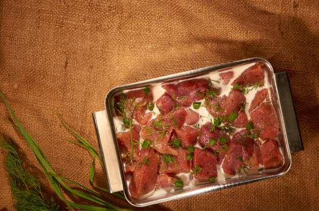 Marinado en leche y hierbas, la carne en una olla de acero sobre la tela con hierbas frescas