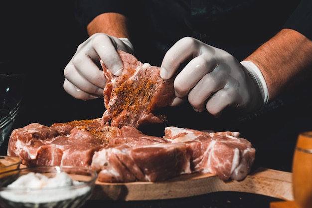 Marinar carne de porco crua para cozinhar espetadas e presunto. O chef do restaurante em luvas trata a carne com manjericão e temperos de curry.